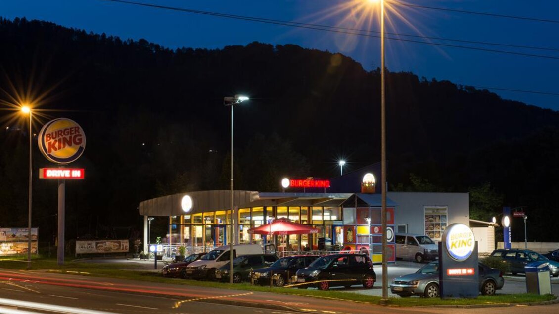 Ein Burger King Restaurant bei Nacht, beleuchtet von Straßenlaternen. Zahlreiche Autos parken vor dem Lokal. | © Fotostudio Helmut Reisinger