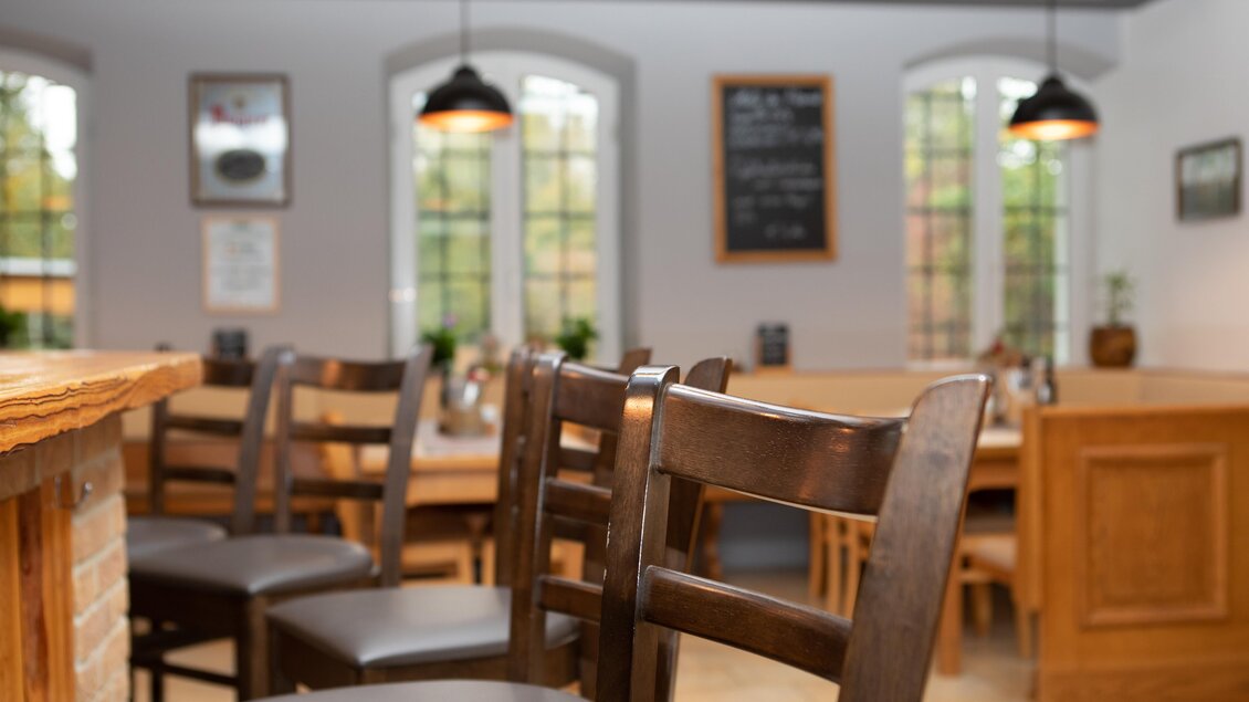 Ein gemütliches Restaurant mit Holzstühlen und einem einladenden Ambiente. Die Fenster lassen viel Licht herein und schaffen eine angenehme Atmosphäre. | © GlaMUR-Genus am Fluss