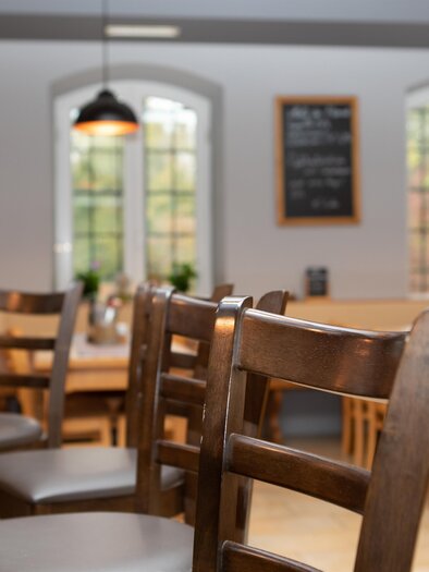 Ein gemütliches Restaurant mit Holzstühlen und einem einladenden Ambiente. Die Fenster lassen viel Licht herein und schaffen eine angenehme Atmosphäre. | © GlaMUR-Genus am Fluss