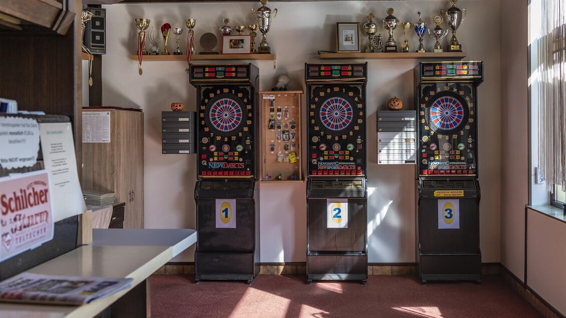 Drei Dartsautomaten stehen in einem Raum mit Holzwänden. An den Wänden hängen Pokale und Auszeichnungen. | © Familie Mutlu