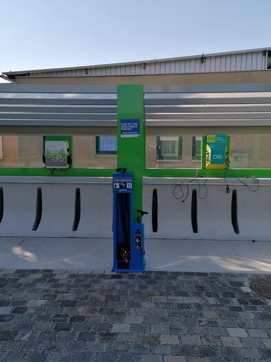 A modern car wash station with a blue control device and green accents. The station is located under a covered area on a paved floor. | © Kurkommission Bad Blumau