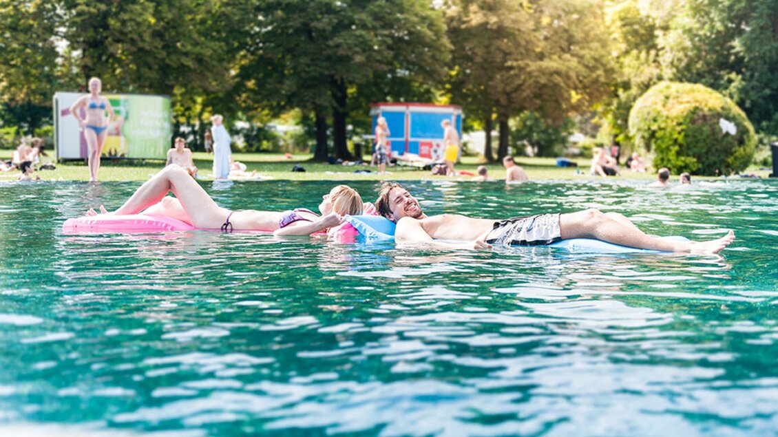 Ein erfrischender Sommertag am Wasser. Zwei Personen relaxen auf Luftmatratzen in einem klaren Wasser im Bad Straßgang in Graz. | © Holding Graz - Joel Kernasenko