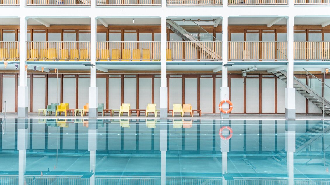 Innenansicht des Hallenbads im Bad zur Sonne mit bunten Liegestühlen in Graz | © Holding Graz - achtzigzehn