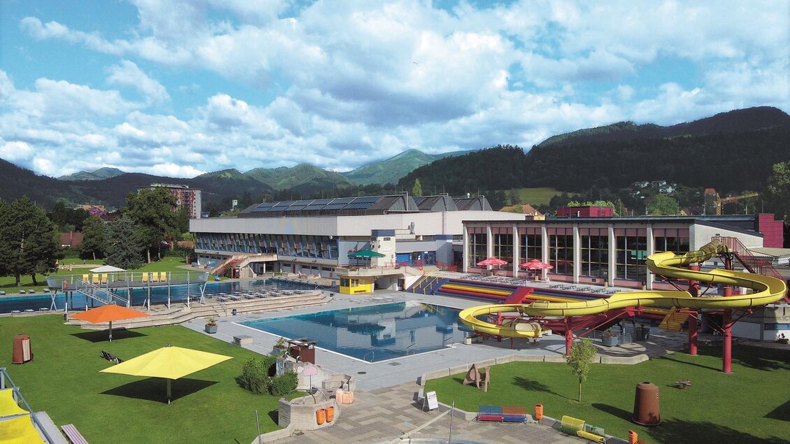 Ein Wasserspaßbad mit großen Schwimmbecken und Rutschen. Die Umgebung ist grün und einladend, ideal für Familien.