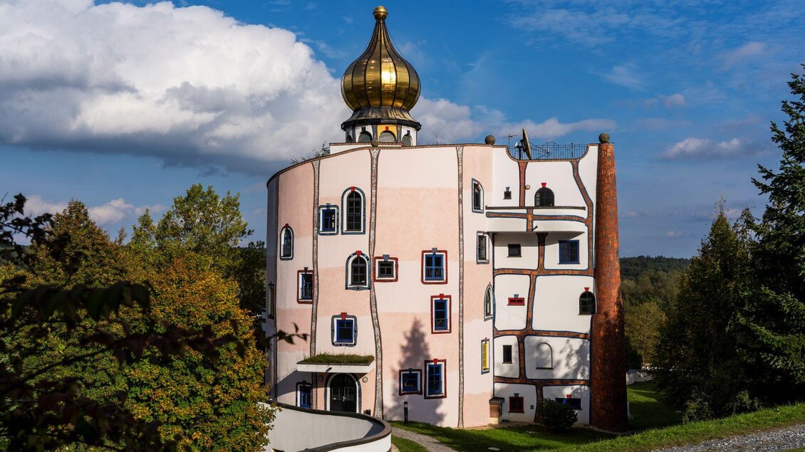 Ein einzigartiges Gebäude mit einer goldenen Kuppel und bunten Fenstern. Es steht in einer grünen Umgebung unter einem blauen Himmel. | © Kurkommission Bad Blumau