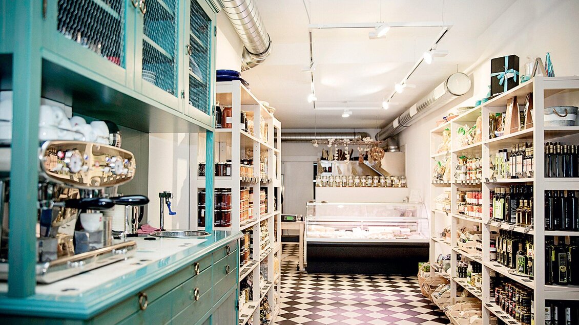 Ein einladender Laden mit hellen Regalen, die verschiedene Lebensmittel und Getränke anbieten. Im Vordergrund steht eine alte Kaffeemaschine und im Hintergrund gibt es eine Kühltheke. | © Bakaliko