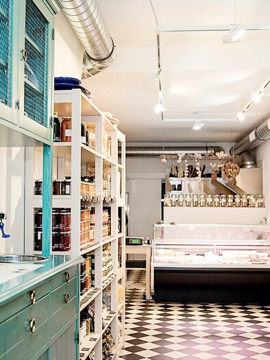 Ein einladender Laden mit hellen Regalen, die verschiedene Lebensmittel und Getränke anbieten. Im Vordergrund steht eine alte Kaffeemaschine und im Hintergrund gibt es eine Kühltheke. | © Bakaliko