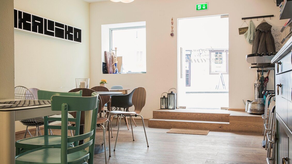 Ein gemütlicher Innenraum mit Tischen und Stühlen in verschiedenen Farben. Ein helles Fenster bietet Blick nach draußen. | © Bakaliko