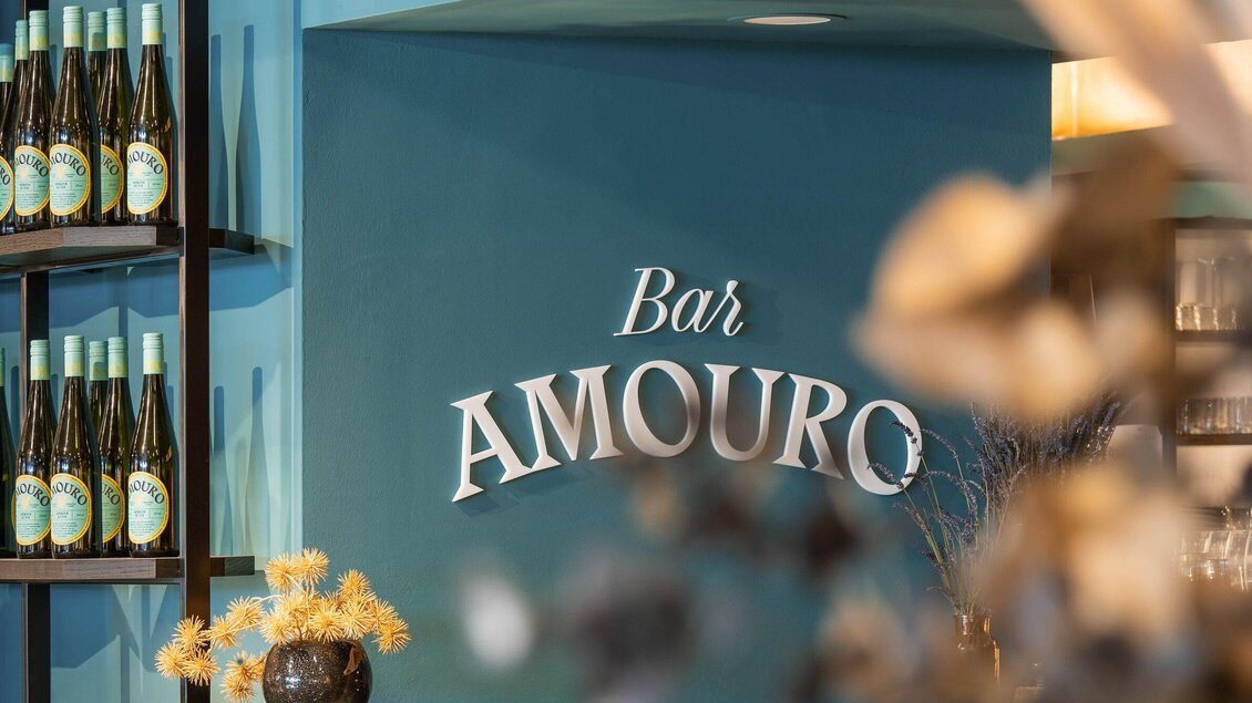 Eine elegante Bar mit dem Namen "Bar AMOURO" und einer blauen Wand. Im Hintergrund sind Flaschen auf Regalen sichtbar. | © Bar Amouro - Lucija Novak