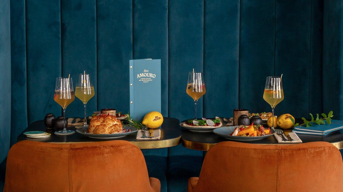 Ein elegantly gedeckter Tisch mit köstlichen Speisen und Getränken. Die Kulisse ist in beruhigenden Blau- und Erdtönen gehalten. | © Bar Amouro - Kristina Sammer