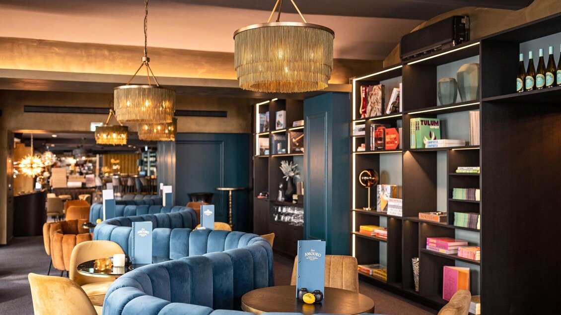 Ein stilvolles Restaurantinterieur mit blauen Sofas und eleganten Beleuchtungskörpern. Bücherregale und dekorative Elemente verleihen dem Raum eine gemütliche Atmosphäre. | © Bar Amouro - Lucija Novak