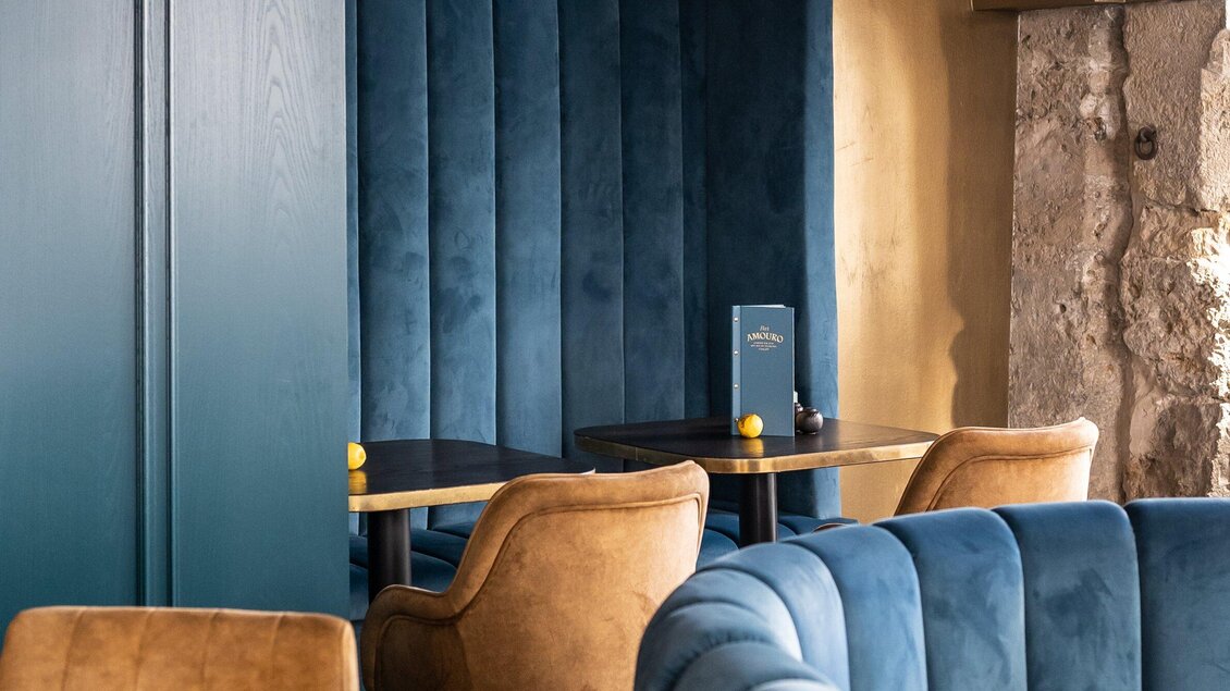 Ein elegantes Restaurant mit blauen Wänden und gemütlichen Sitzgelegenheiten. Ein Tisch befindet sich zwischen den Sesseln, dekoriert mit einer kleinen Speisekarte. | © Bar Amouro - Lucija Novak