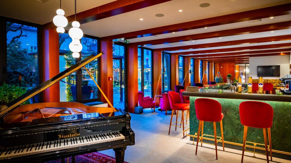 Flügel mit Teppich und grüne Bar mit roten Hockern vor Fensterfront. | © Parkhotel Graz