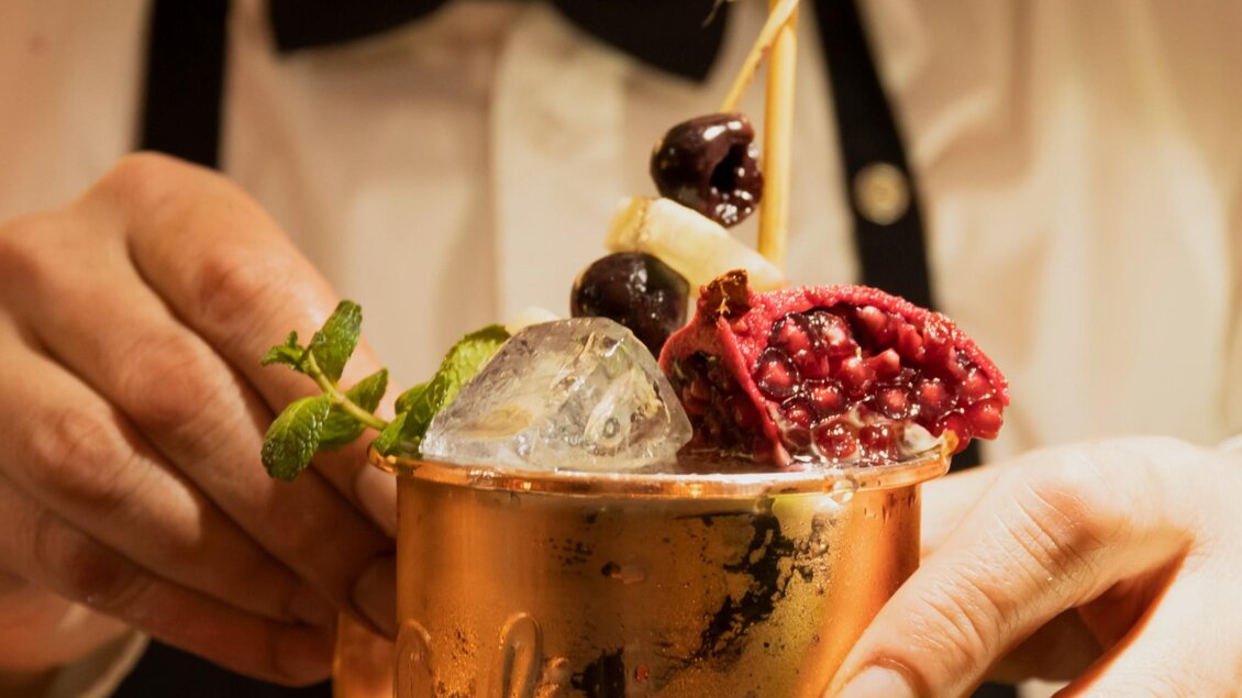 Ein Cocktail in einem Kupferbecher mit frischen Früchten und Minze. Der Drink wird von einer Hand gehalten und enthält Eiswürfel. | © Magdalena Bereznicka