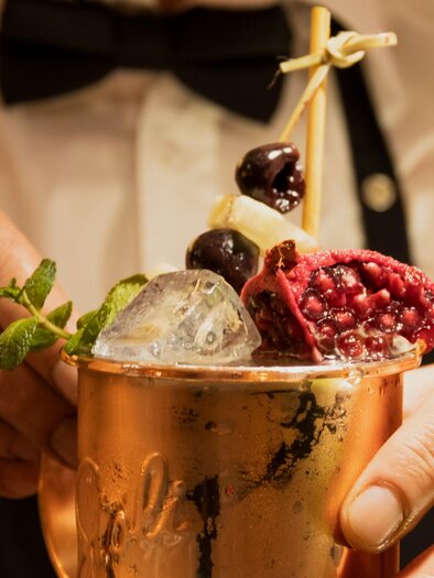 Ein Cocktail in einem Kupferbecher mit frischen Früchten und Minze. Der Drink wird von einer Hand gehalten und enthält Eiswürfel. | © Magdalena Bereznicka