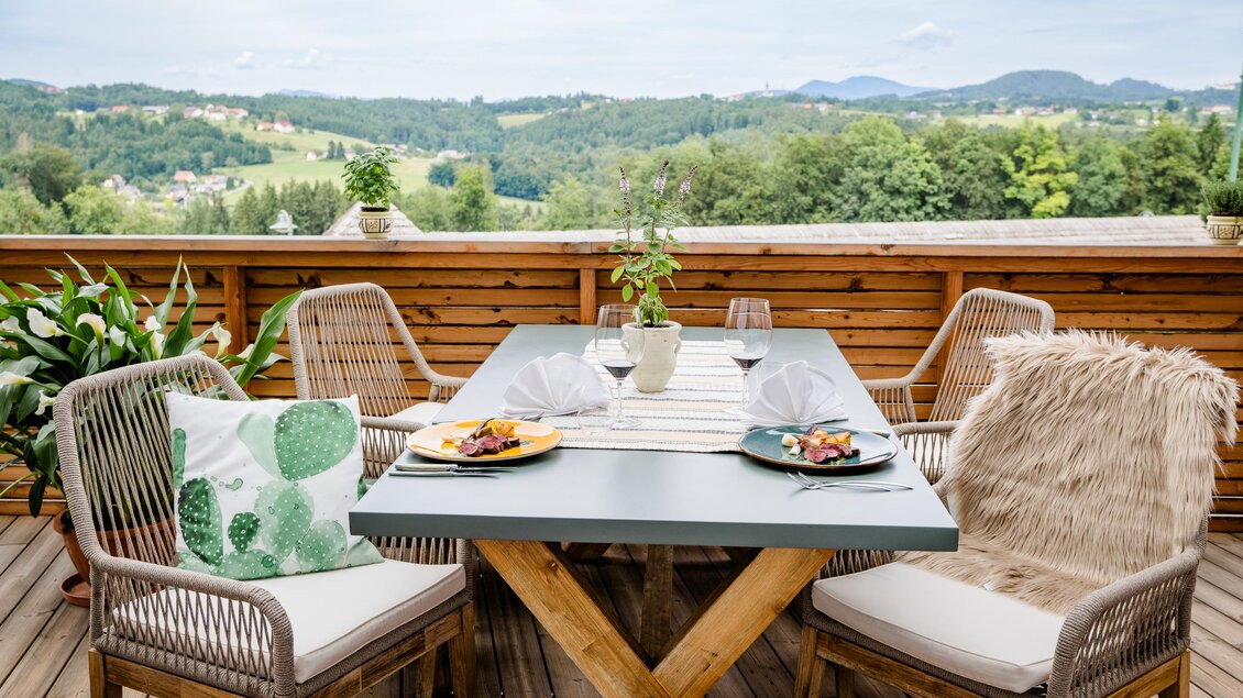 Ein einladender Esstisch auf einer Terrasse mit Blick auf die Berge. Stühle und Dekoration sorgen für eine gemütliche Atmosphäre. | © Steiermark Tourismus - STG
