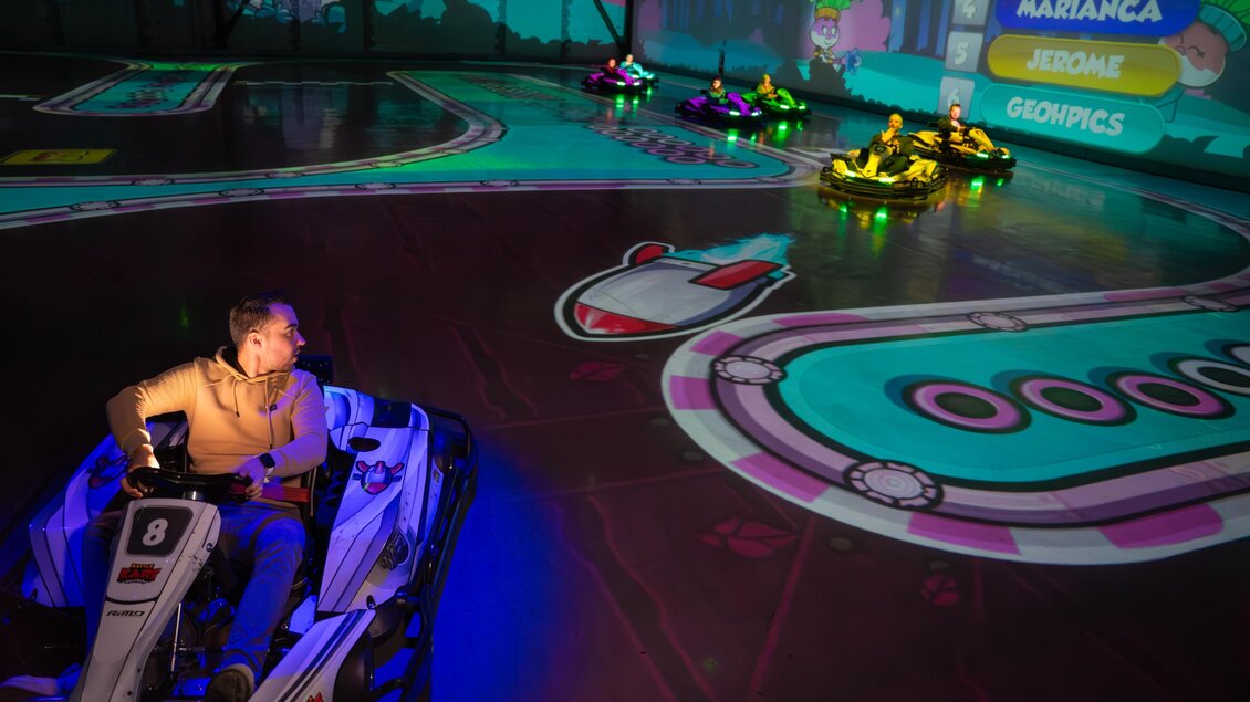 Fahrer in Elektro-Karts auf einer Halle mit bunt projizierter Rennstrecke, farbigen Lichtspielen und digitalen Spielelementen | © Battlekart Gössendorf - Stefan Novotny