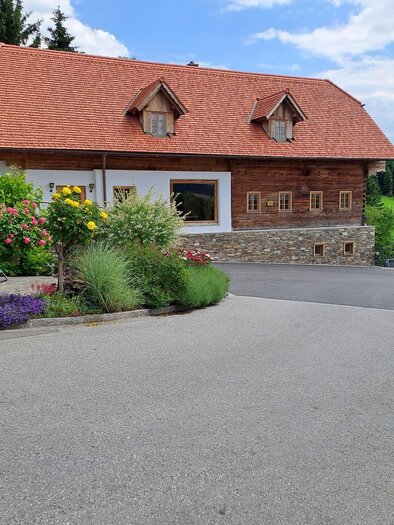 Ein schönes, rustikales Haus mit rotem Dach und grünen Wiesen im Hintergrund. Bunte Blumen schmücken den Weg zum Haus. | © Familienbetrieb Buchegger