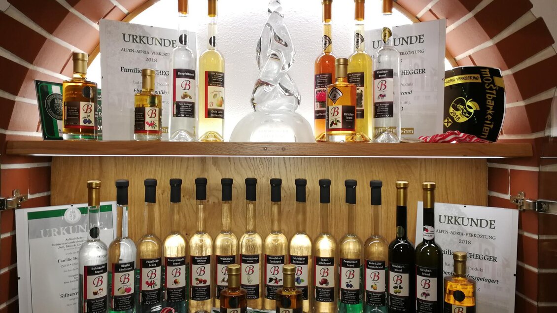 Ein Regal mit verschiedenen Flaschen alkoholfreier Getränke und Auszeichnungen. Im Hintergrund gibt es eine dekorative Statue. | © Bauernhof Buchegger