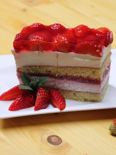 Ein Stück Erdbeertorte mit mehreren Schichten und frischen Erdbeeren. Die Torte hat eine glatte Creme und eine glänzende Erdbeerglasur. | © Bauernhofbackstube Rössing