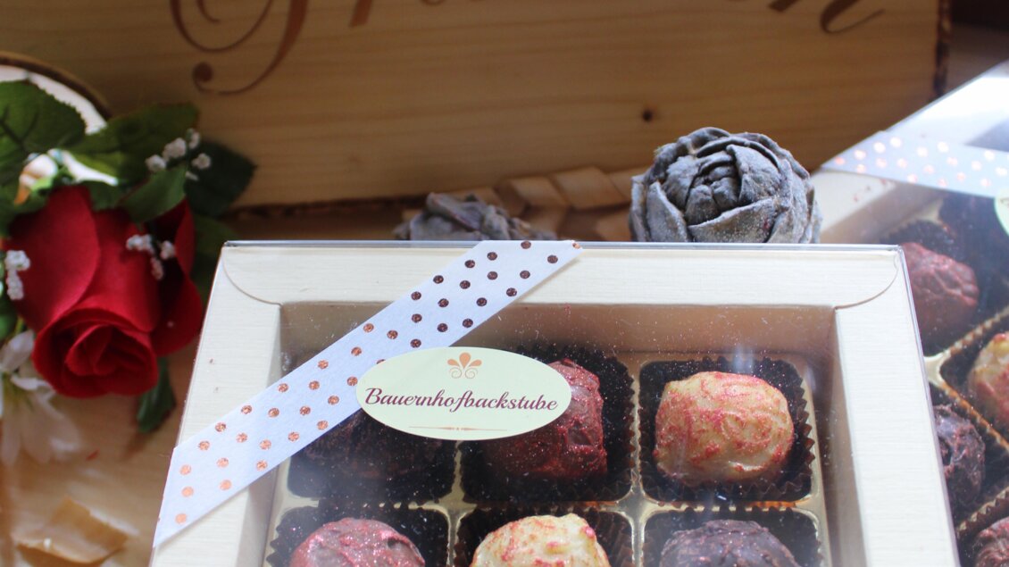 Eine Box mit handgefertigten Pralinen in verschiedenen Farben. Im Hintergrund steht ein Holzschild mit der Aufschrift "Zirben Pralinen". | © Bauernhofbackstube Rössinger