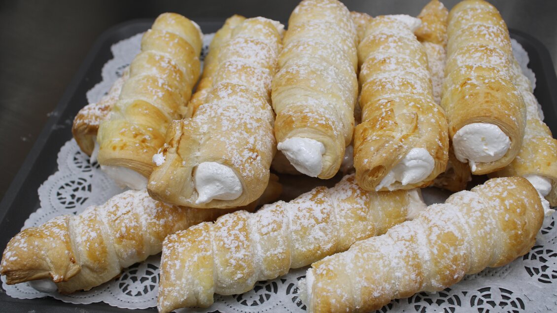 Leckere Gebäckstücke auf einem Tablett. Sie sind mit Zucker bestaubt und gefüllt mit Sahne. | © Bauernhofbackstube Rössinger