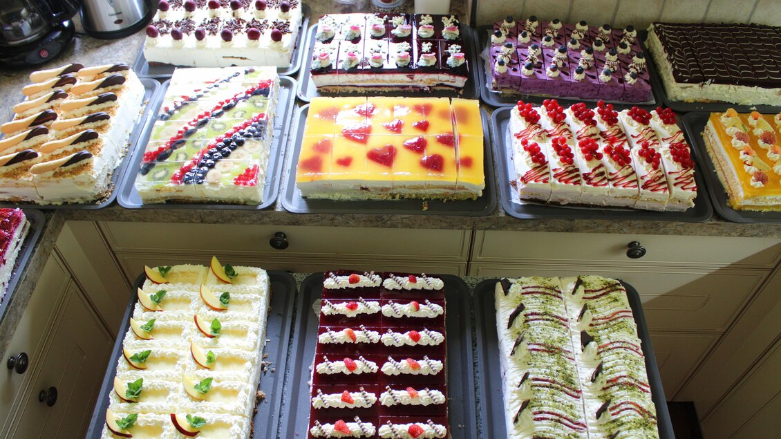 Eine Vielzahl von bunten Kuchen und Torten auf mehreren Blechen. Die Leckereien sind mit Sahne und frischen Früchten dekoriert. | © Bauernhofbackstube Rössinger