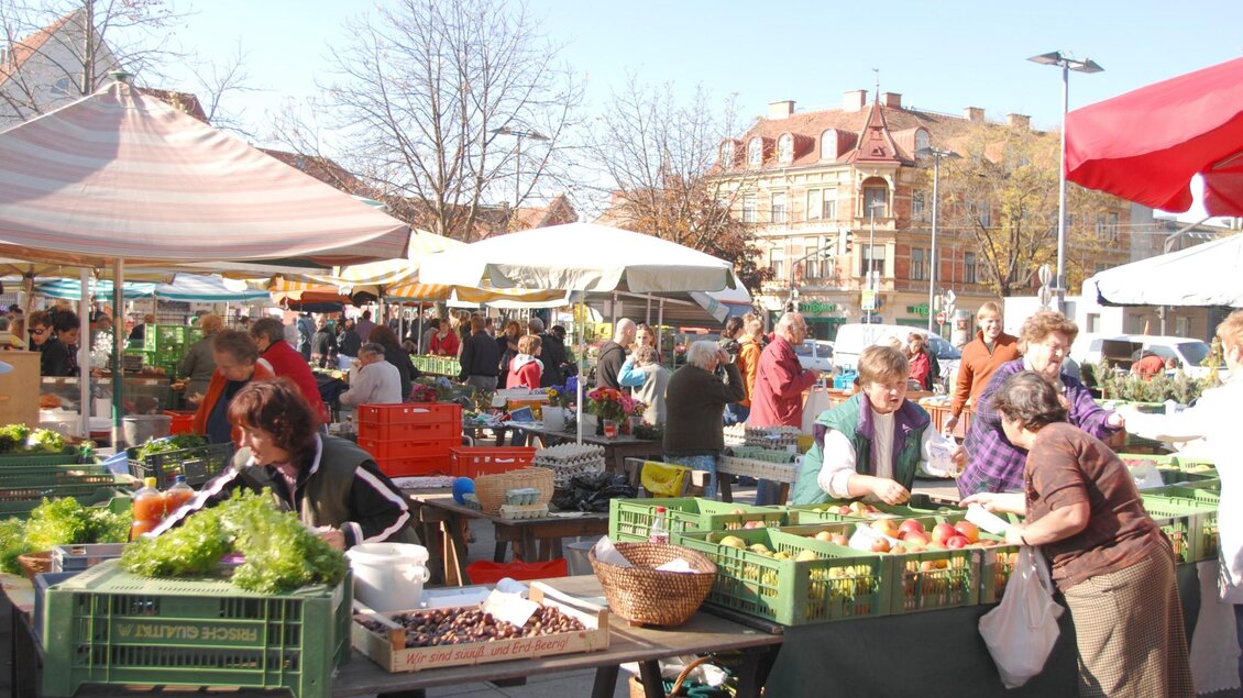 Zahlreiche Menschen kaufen an Marktständen mit Gemüse, Obst und Kräutern unter Sonnenschirmen ein | © Graz Tourismus - icegirl