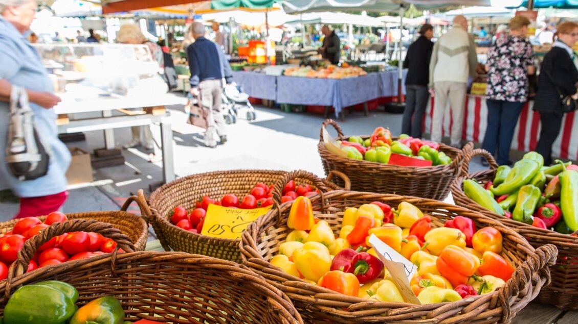 Körbe mit bunten Paprika und Tomaten auf einem Marktstand, im Hintergrund Menschen beim Einkaufen | © Graz Tourismus - Harry Schiffer