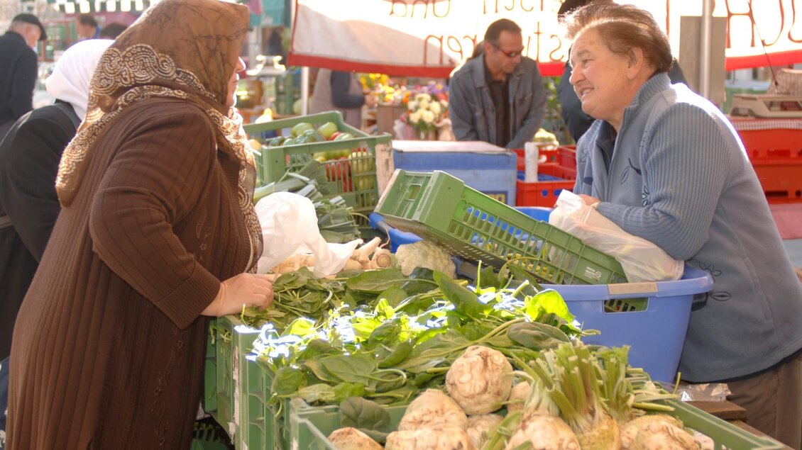 Zwei Frauen im Gespräch an einem Marktstand mit frischem Gemüse und Kräuterkisten | © Graz Tourismus - icegirl