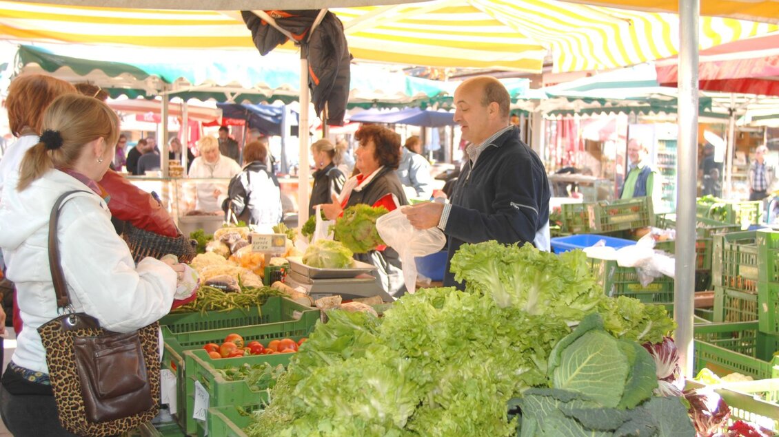 Verkäufer reicht Kundin Gemüse über den Marktstand mit Salat, Kohl und Tomaten | © Graz Tourismus - icegirl
