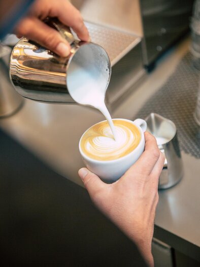 A hand pours frothed milk into a cup of coffee. The coffee has a beautiful latte art surface. | © Bellaggio