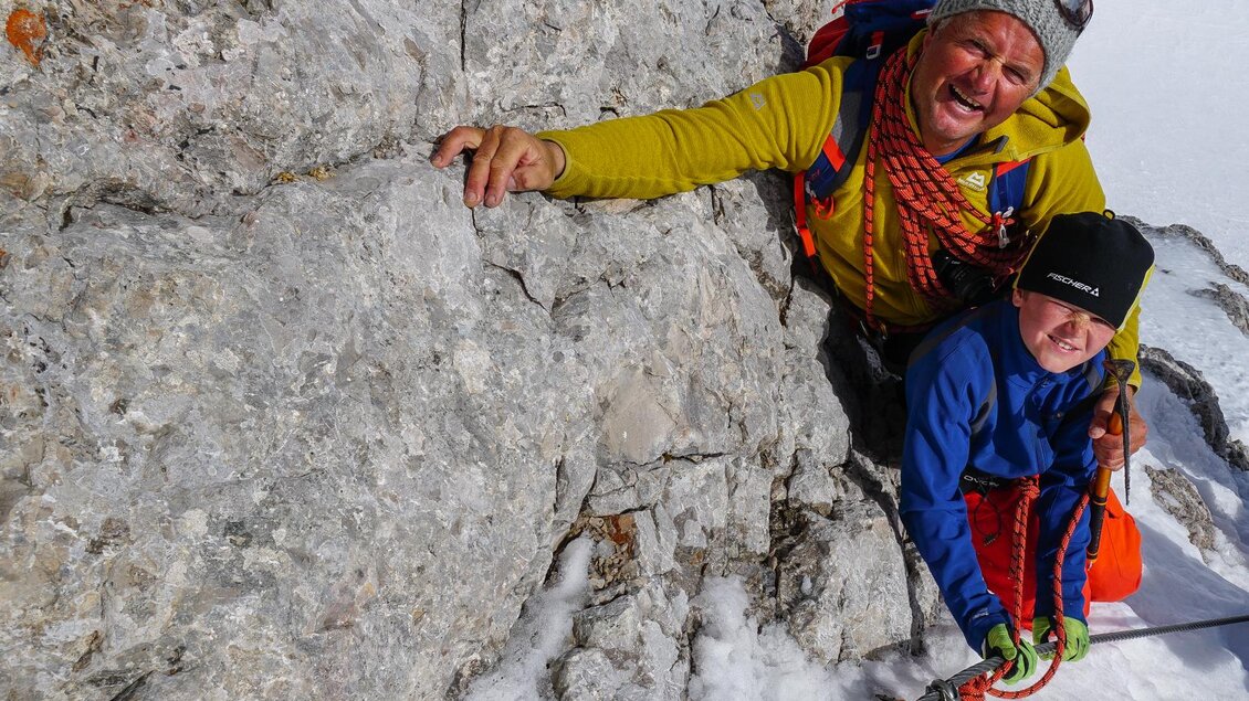 Ein Bergsteiger mit einem Kind klettert an einer steilen Felswand. Beide lächeln und sind mit Sicherheitsharnessen und Seilen gesichert. | © SODAMIN Paul