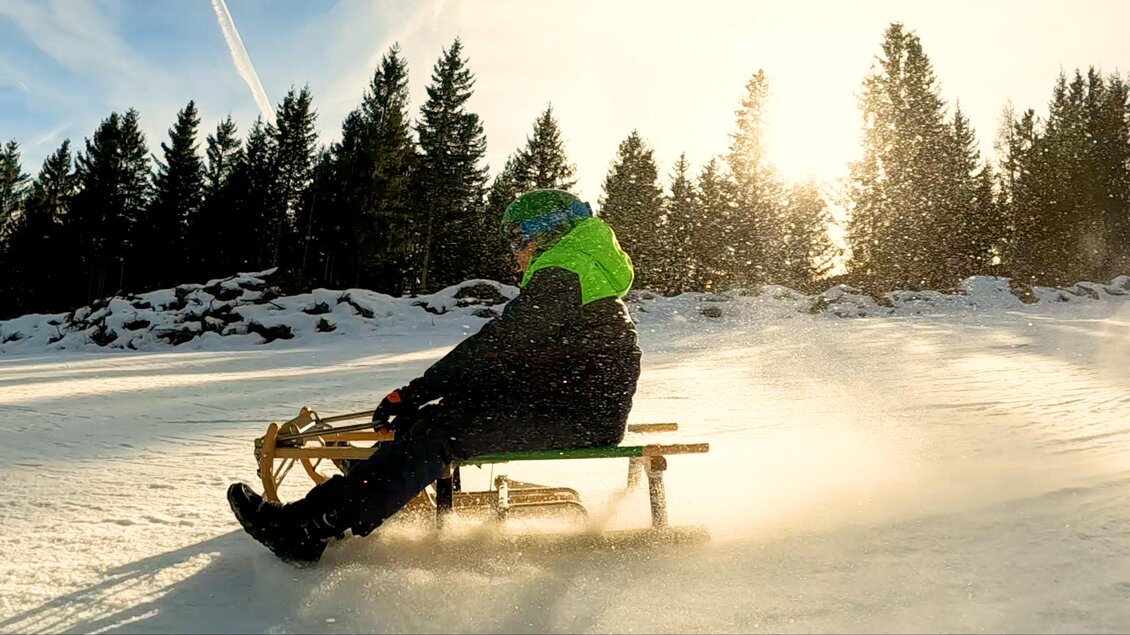 Ein Schlittenfahrer fährt schnell über den Schnee. Im Hintergrund sind Bäume und die Sonne, die eine winterliche Stimmung schafft. | © Rieseralm