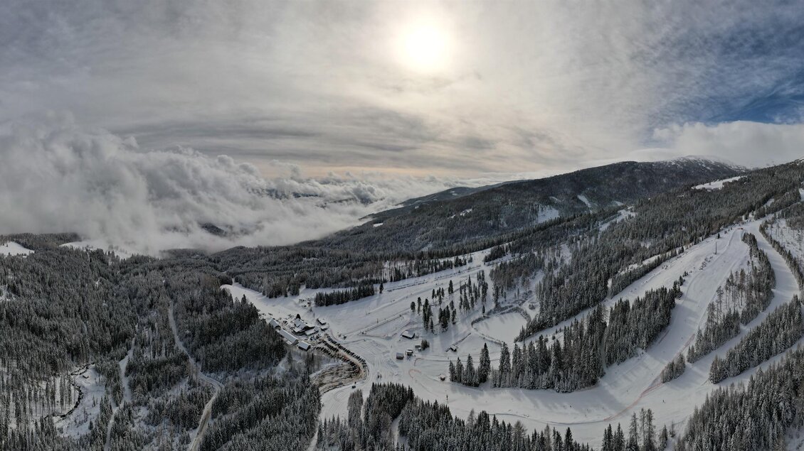 Eine winterliche Landschaft mit schneebedeckten Bergen und einer tiefen Wolkendecke. Die Sonne strahlt über die beeindruckende Bergkulisse. | © Rieseralm