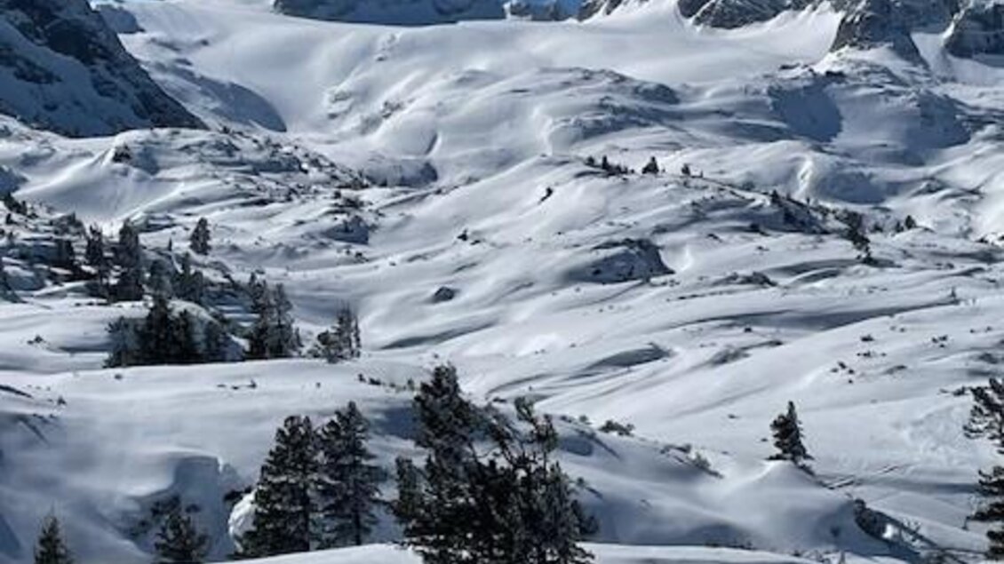 Eine verschneite Berglandschaft mit hohen Gipfeln und klarem Himmel. Zwei Personen gehen auf einem schneebedeckten Weg. | © Walter Walcher