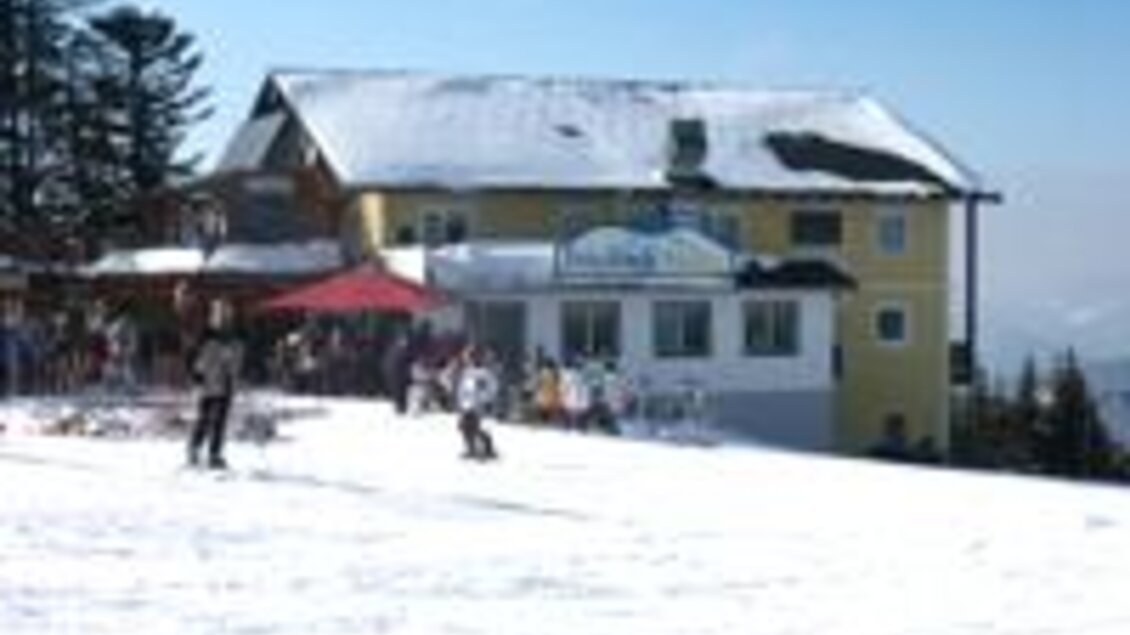 Ein schneebedeckter Hang mit einem großen, gelben Gebäude im Hintergrund. Skifahrer und Besucher genießen die Winterlandschaft. | © Fam. Filzwieser