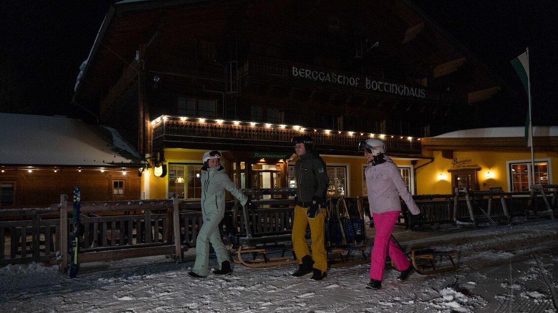 Eine Gruppe von drei Personen steht vor einem Chalet im Schnee. Es ist Nacht und das Gebäude ist schön beleuchtet. | © Harald Steiner
