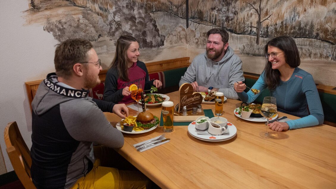 Eine Gruppe von vier Personen sitzt an einem Tisch und genießt eine Mahlzeit in einem gemütlichen Restaurant. Es gibt verschiedene Gerichte und Getränke auf dem Tisch. | © Harald Steiner