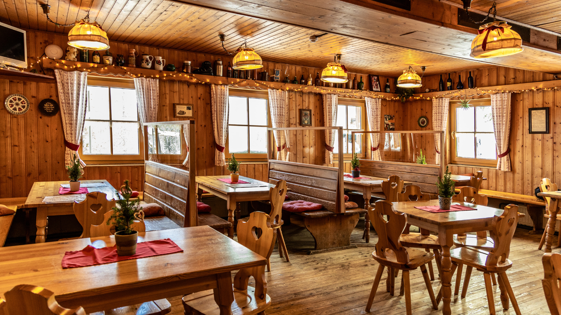 Ein gemütliches Restaurant mit Holzmöbeln und warmem Licht. Es gibt Tische mit Blumendekoration und große Fenster, die für eine einladende Atmosphäre sorgen. | © Berggasthof Hollhaus, needful.at