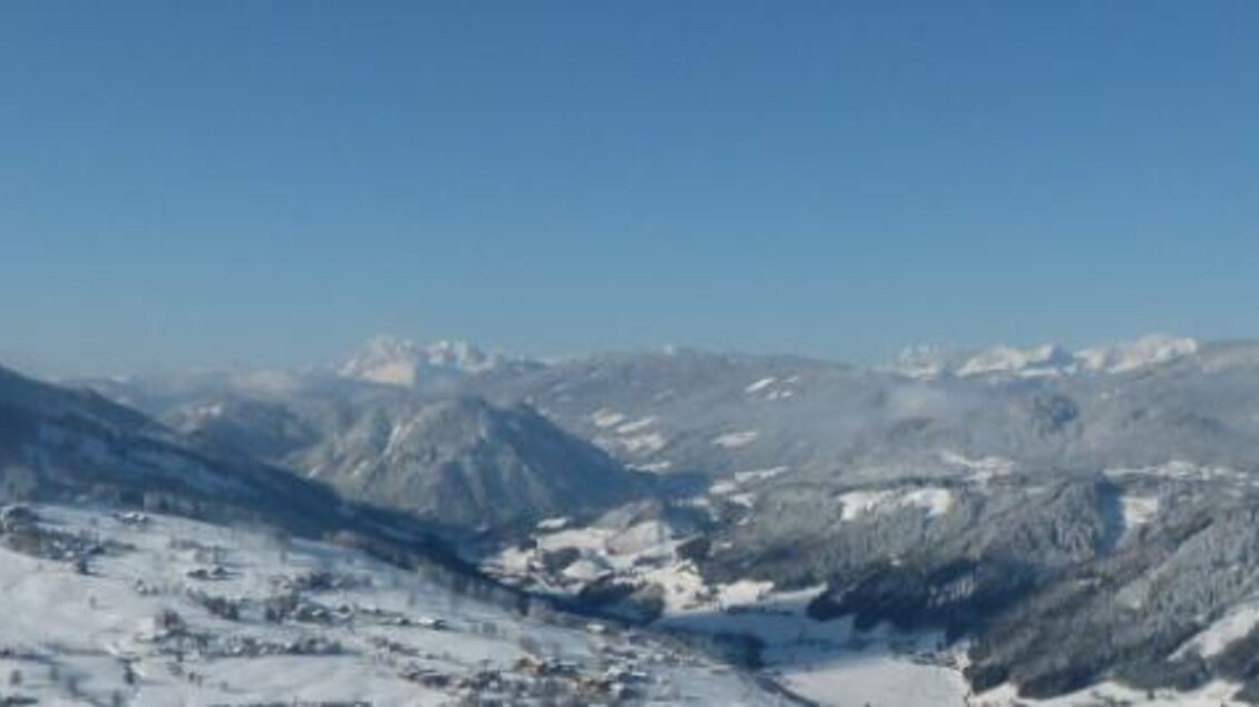 Eine majestätische Berglandschaft im Winter mit schneebedeckten Gipfeln und einem klaren blauen Himmel. Im Vordergrund ist ein Tal mit schneebedeckten Bäumen zu sehen. | © Berggasthof Jager GmbH