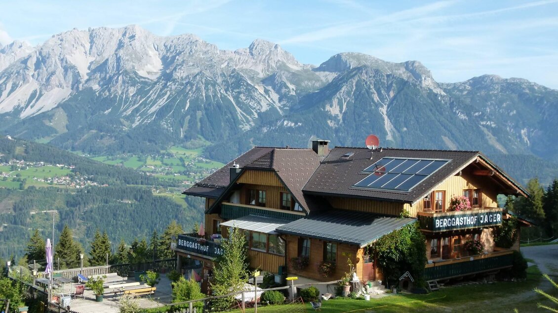 Ein gemütliches Bergrestaurant liegt in der malerischen Landschaft. Im Hintergrund erheben sich majestätische Berge unter einem klaren Himmel. | © Berggasthof Jager