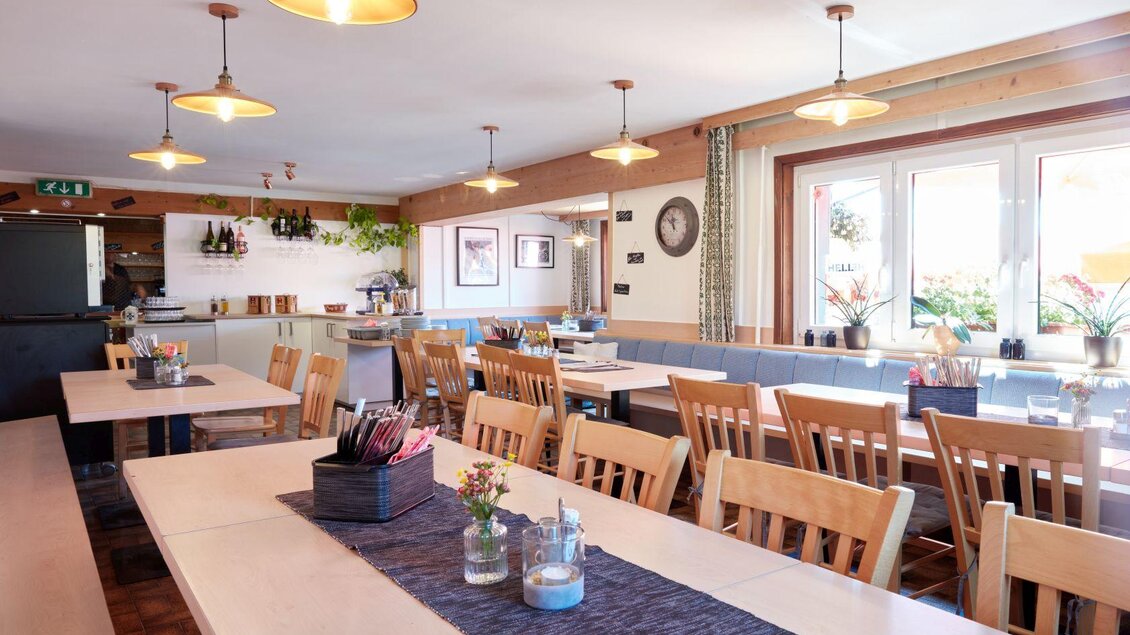 Ein einladendes Restaurant mitHolztischen und Stühlen. Die Wände sind mit Pflanzen und Bildern dekoriert, und es gibt viel Tageslicht durch die Fenster. | © Karin Klammer Fotografie