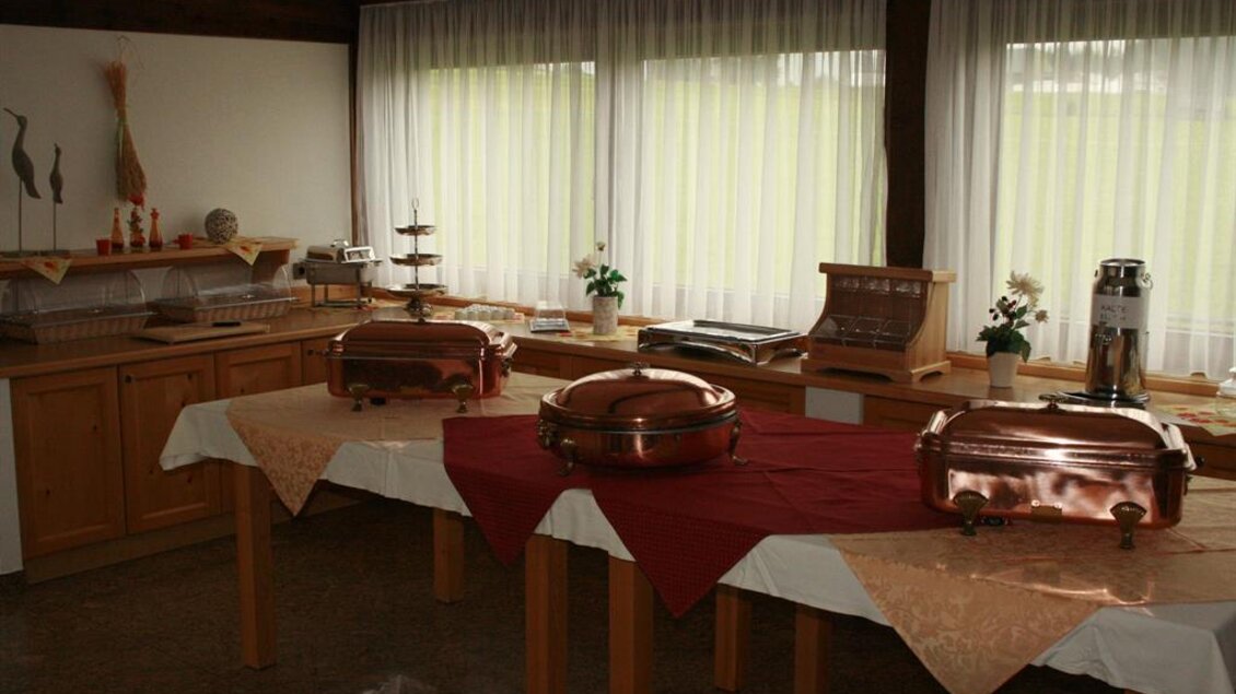 Ein gemütlicher Raum mit großen Fenstern, der für eine Veranstaltung vorbereitet ist. Auf den Tischen stehen mehrere Buffetbehälter und dekorative Elemente. | © Berghof Mitterberg