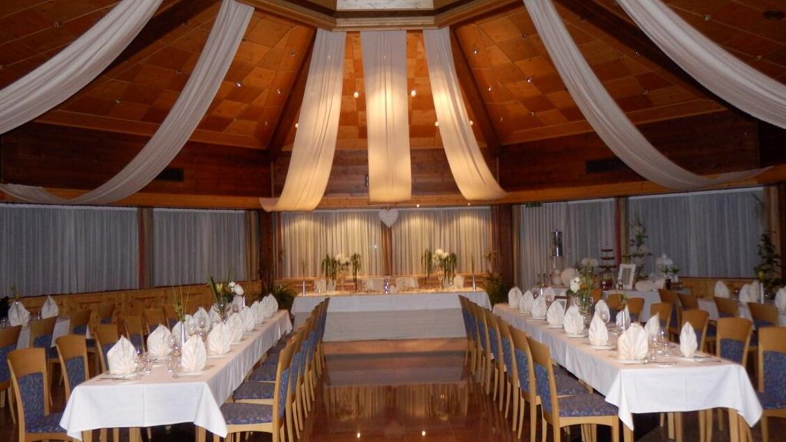Ein elegant dekorierter Festsaal mit langen Tischen und weißen Tischdecken. Im Hintergrund sind Blumenarrangements und sanfte Beleuchtung zu sehen. | © Berghof Mitterberg