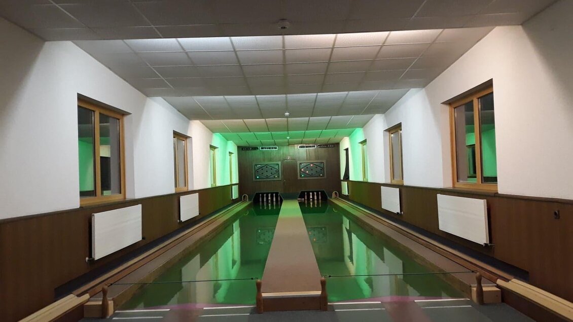 Eine Kegelbahn mit grünem Licht und glatten Holzoberflächen. Die Wände sind hell und die Atmosphäre ist einladend. | © Berghof Mitterberg 