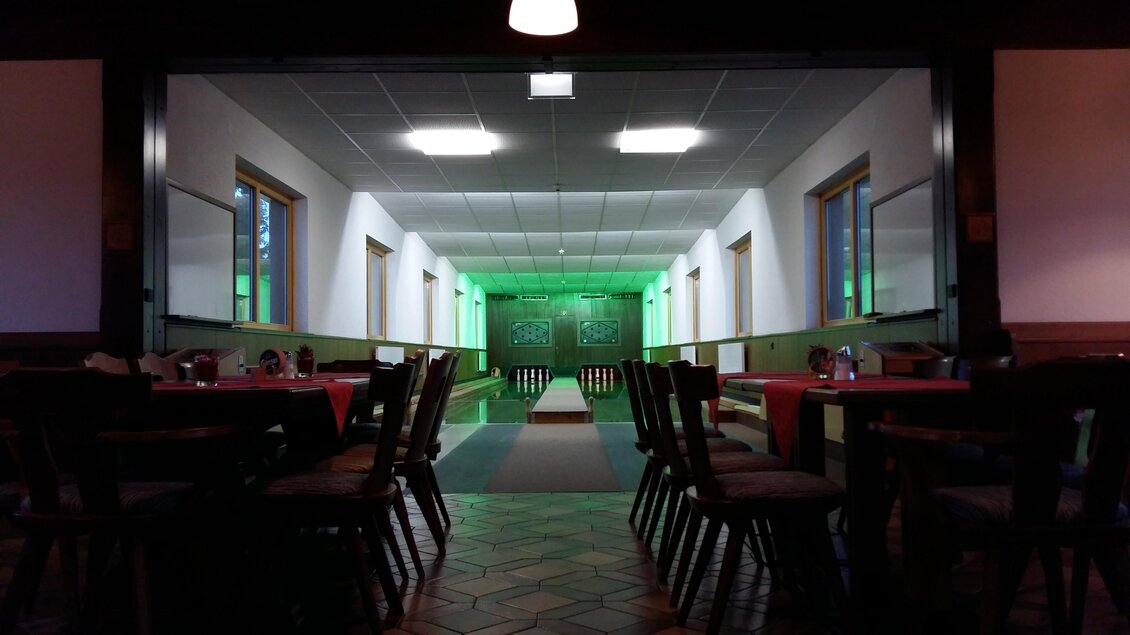 Ein Restaurant mit langen Tischen und einer breiten, beleuchteten Gasse im Hintergrund. Die Wände sind mit grünen Lichtern dekoriert. | © Berghof Mitterberg 