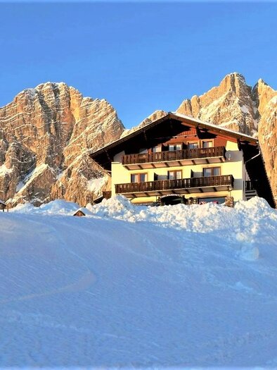 A beautiful chalet in the snow, surrounded by impressive mountains. The sky is clear and the sun is shining. | © Berghotel Türlwand