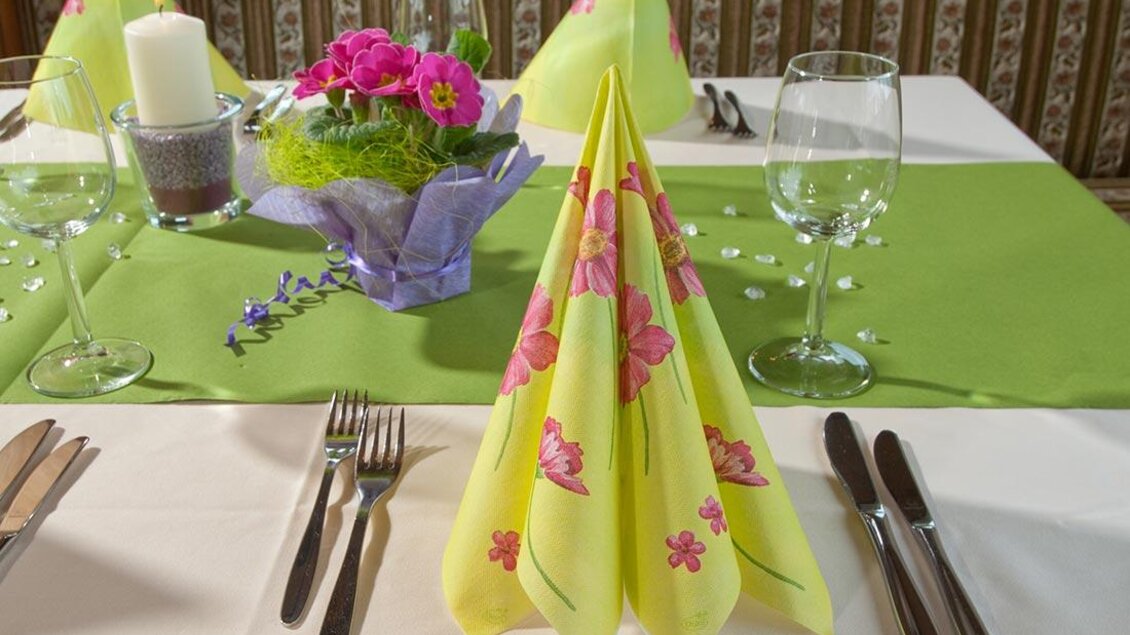 Ein schön gedeckter Tisch mit bunten Servietten und Gläsern. In der Mitte steht ein Blumenarrangement auf einem grünen Tischdecken. | © Berghotel Türlwand