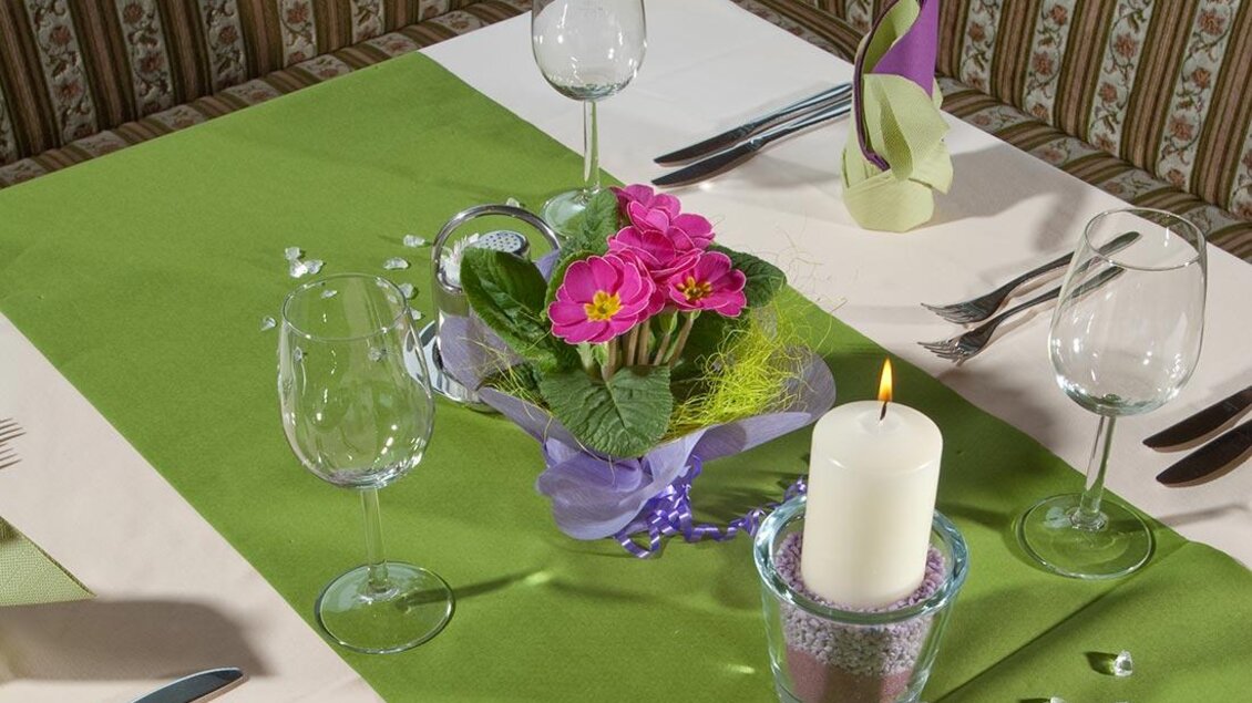 Ein schön gedeckter Tisch mit grüner Tischdecke, Gläsern und einer kleinen Blumenarrangierung. In der Mitte steht eine Kerze in einem dekorativen Halter. | © Berghotel Türlwand